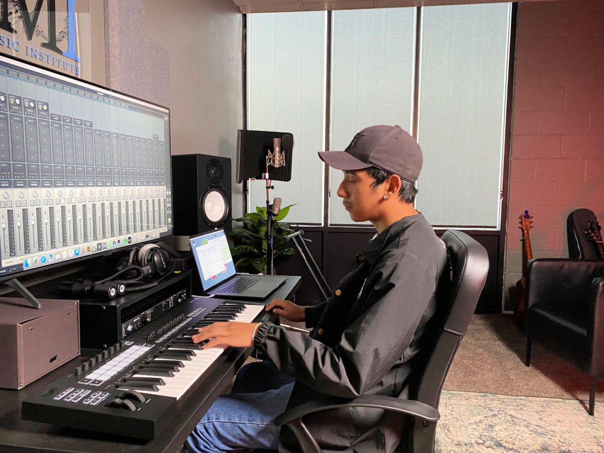 A production student using a keyboard, laptop, and studio microphone during a program created to support music education access.
