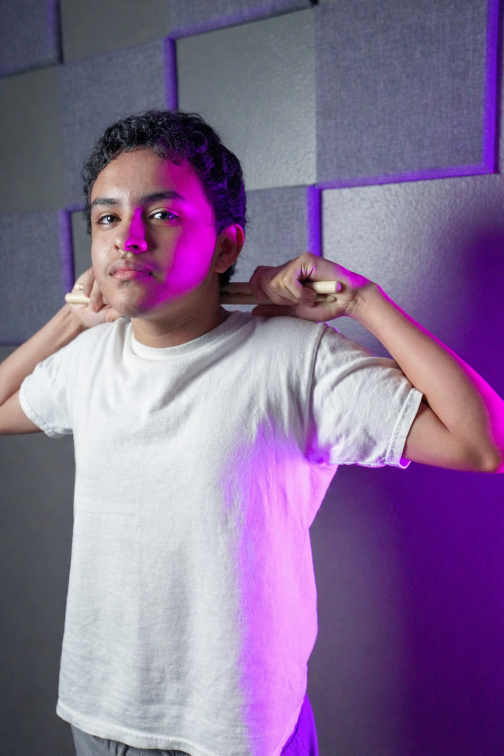 Young male musician holding drumsticks behind his head in a professional recording studio.