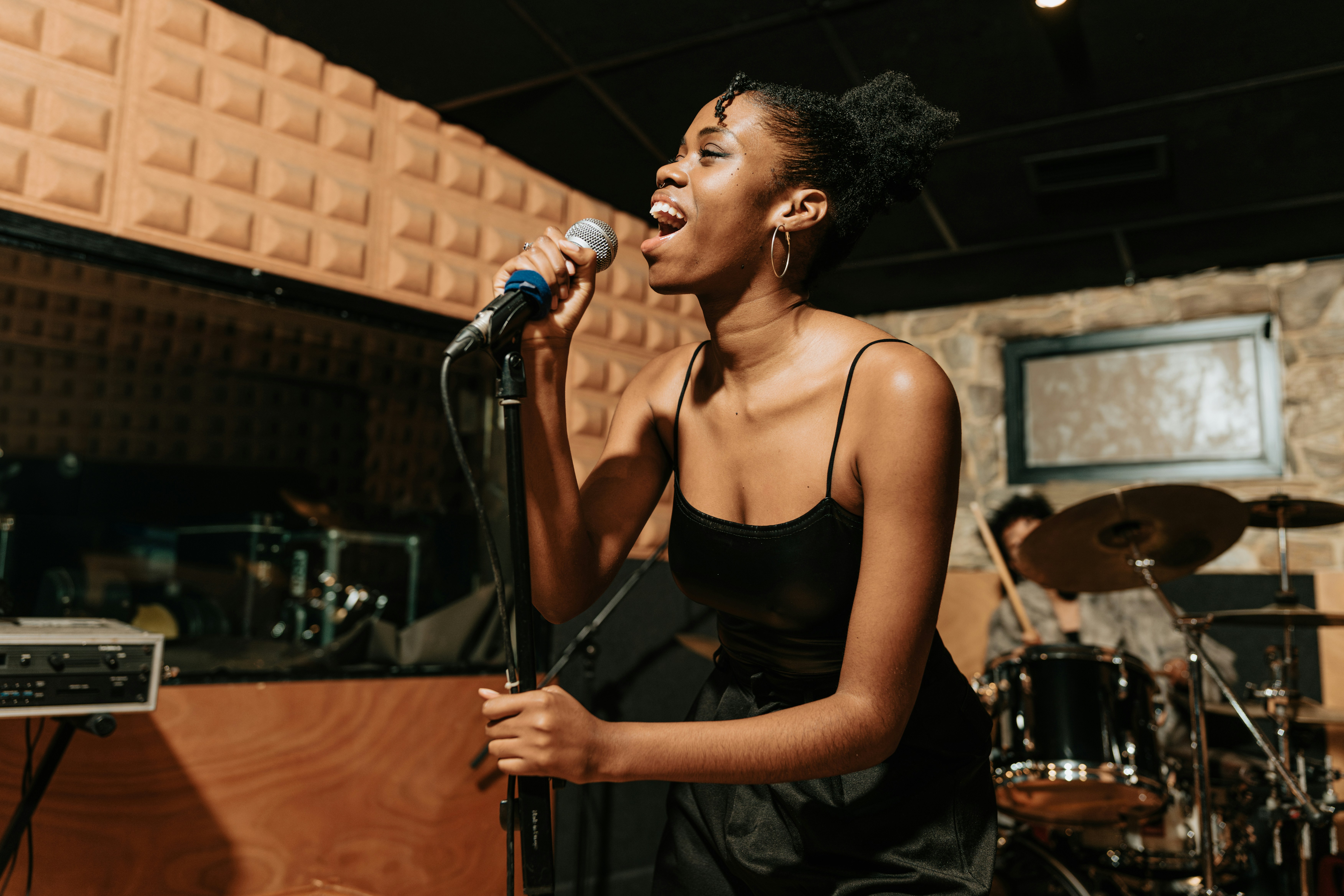 Young female student singing into a handheld microphone in front of a drum kit during a studio session.